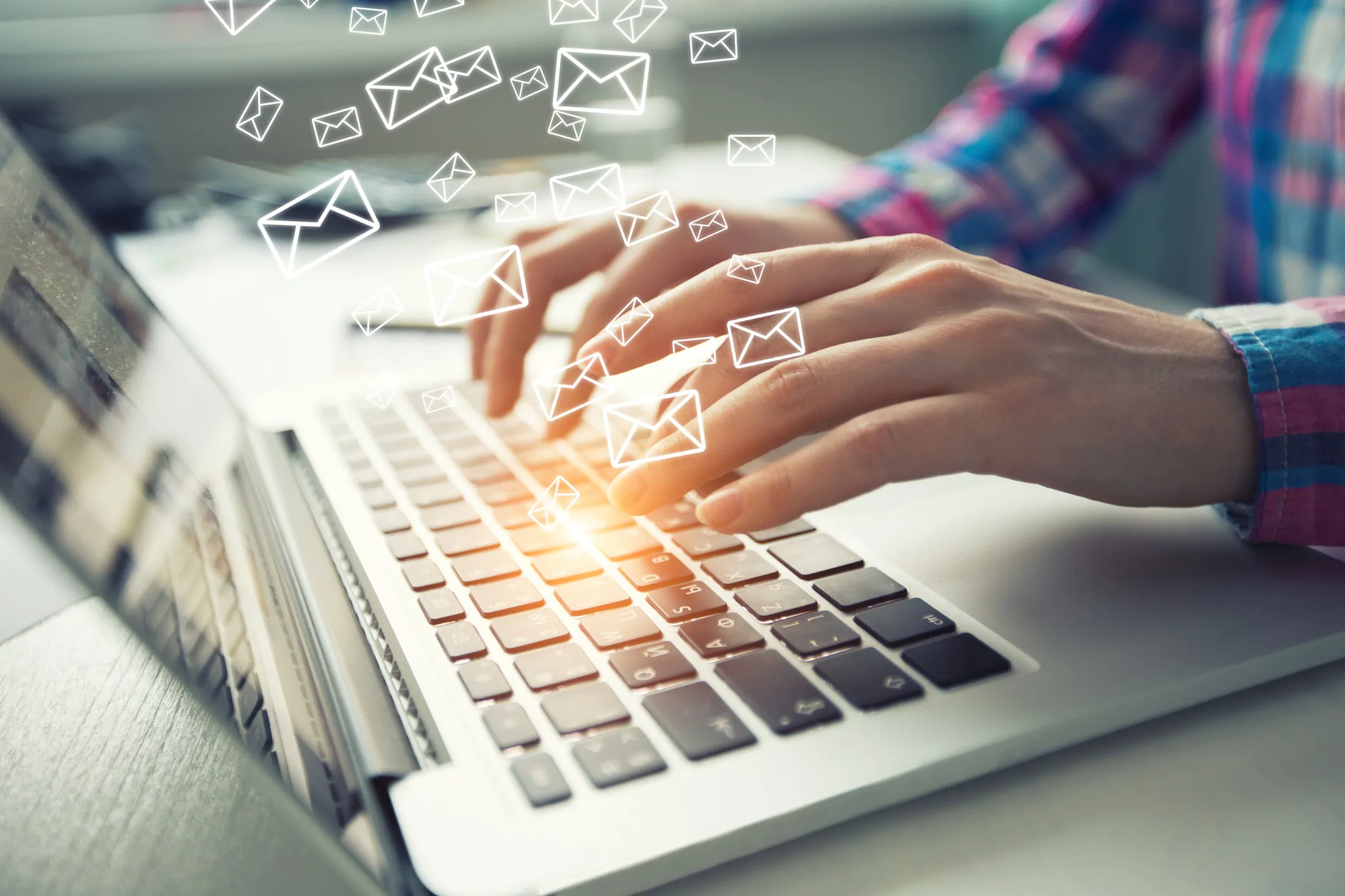 Person using a laptop for email marketing automation with email graphics coming from the keyboard.